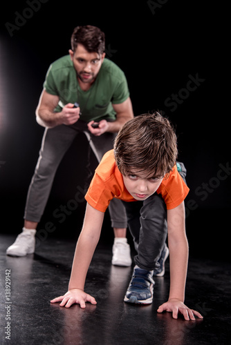 man controlling time while boy training and looking to camera on black