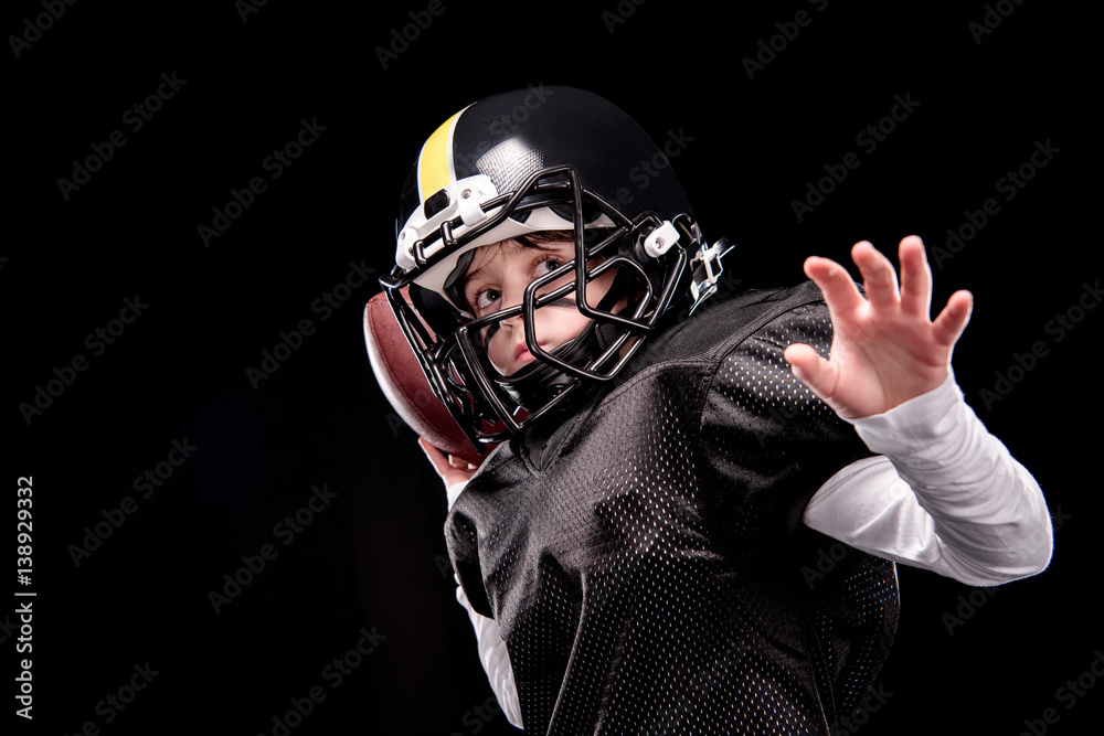 Little boy american football player in uniform throwing ball on black Little boy american football player in uniform throwing ball on black