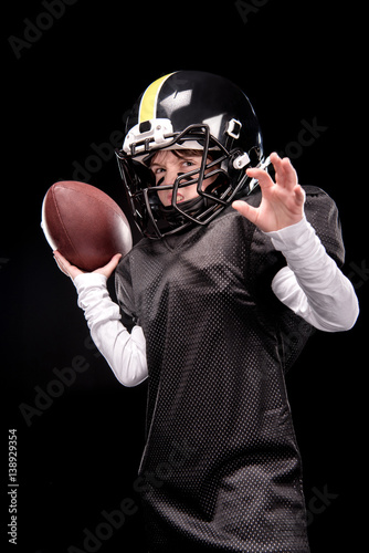 Angry little boy in uniform playing american football on black