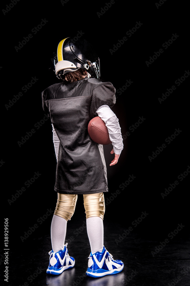 Back view of little boy american football player in uniform holding ball