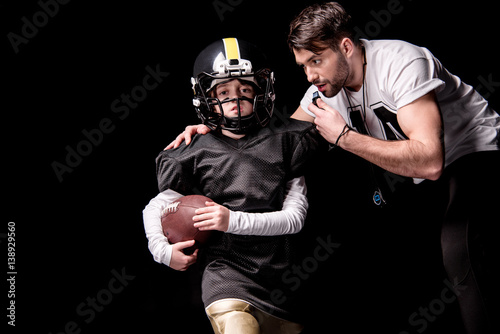 Coach looking at boy american football player running with ball