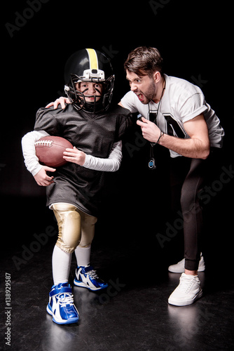 Trainer screaming at boy playing american football on black