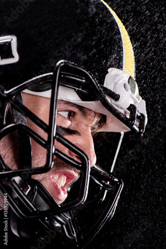 Close-up side view of angry man american football player in helmet on black
