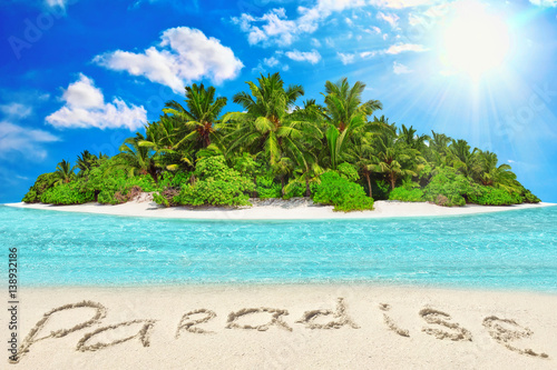 Whole tropical island within atoll in tropical Ocean and inscription "Paradise" in the sand on a tropical island.