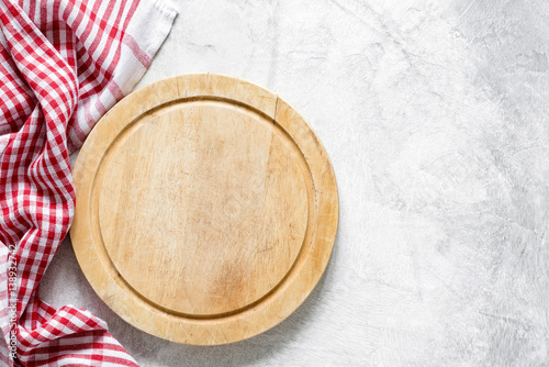 Old round wooden cutting board and red checkered tablecloth on gray concrete background with copy space for text. Cooking food, kitchen utensil, food background. Top view, Horizontal image