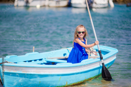 Cute girl in blue boat in the sea bay near the town of Mykonos in Greece. Little kid enjoy swimming in the small boat. © travnikovstudio