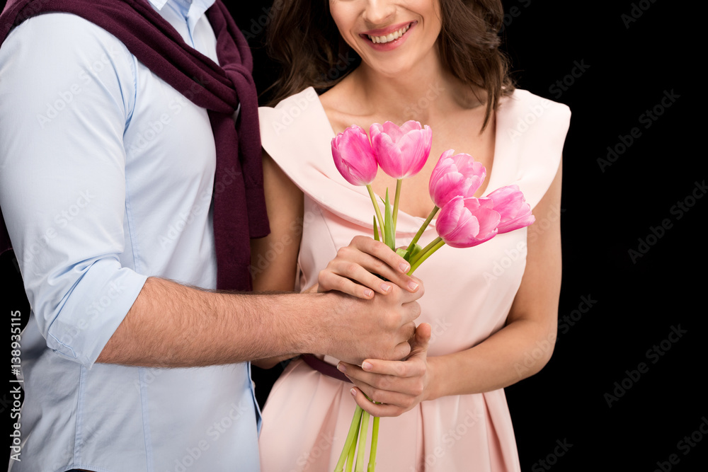 partial view of man presenting tulips bouquet to smiling woman on black, international womens day concept partial view of man presenting tulips bouquet to smiling woman on black, international womens day concept