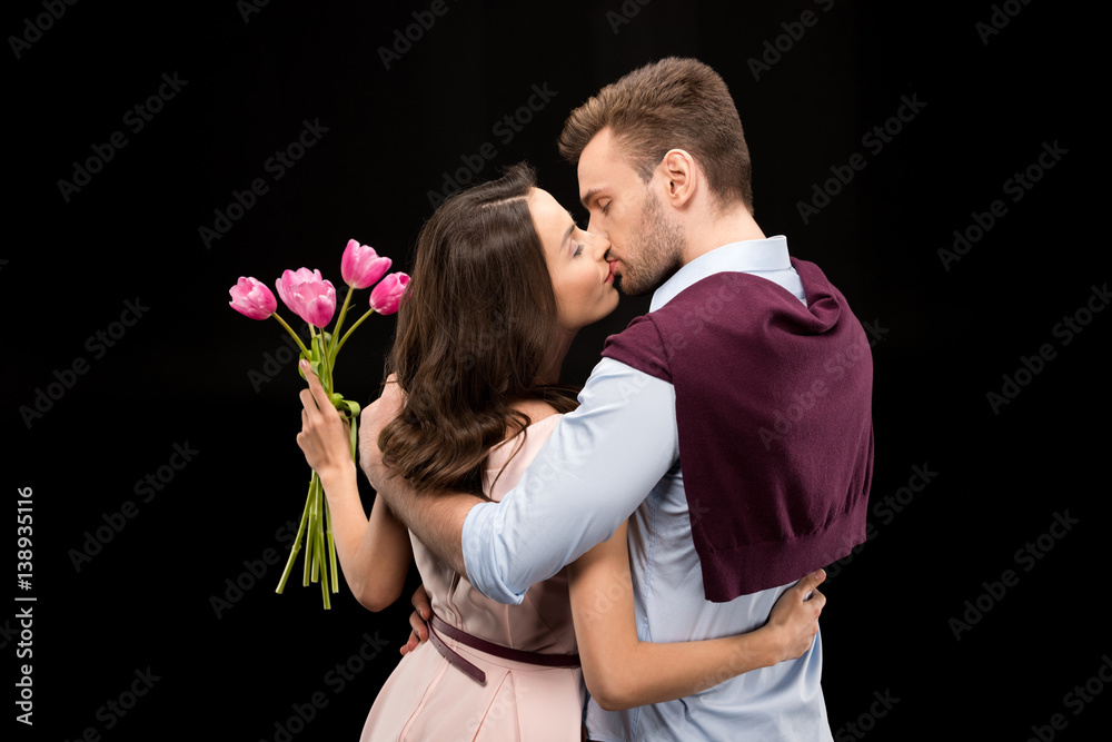 back view of man kissing woman with tulips bouquet on black, international womens day concept back view of man kissing woman with tulips bouquet on black, international womens day concept