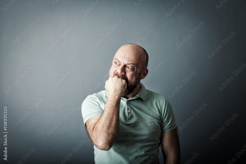 Angry irritated aggressive bearded middle-aged man in plaid shirt biting his fist