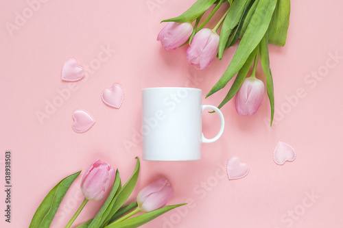 White coffee mug with pink tulips and hearts ona pink background. Space for text or design.