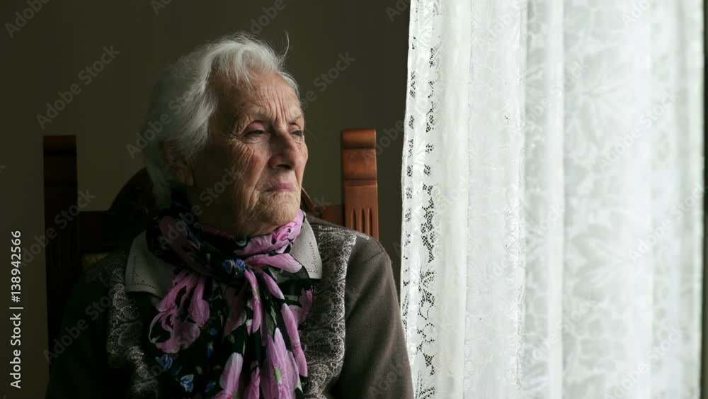  sad and pensive old woman sitting near the window