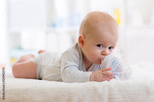sweet baby holding bottle and drinking water in nursery