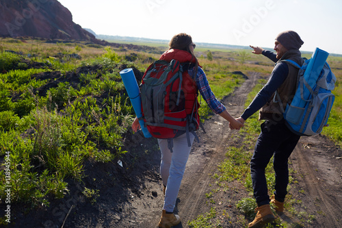 Rear view image of young tourist couple walking on path towards mountains holding hands on sunny day