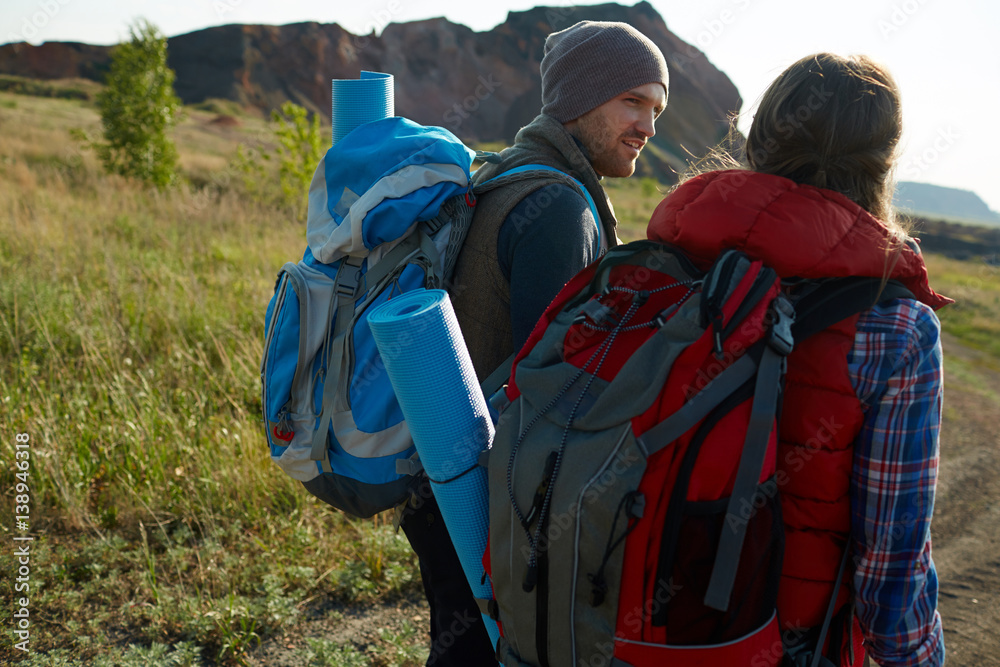 Young couple with big tourist backpacks travelling together in exploring lowland of mountains