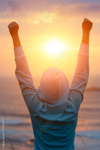 Rear view of motivated woman celebrating workout goals towards the sun. Morning healthy training success.