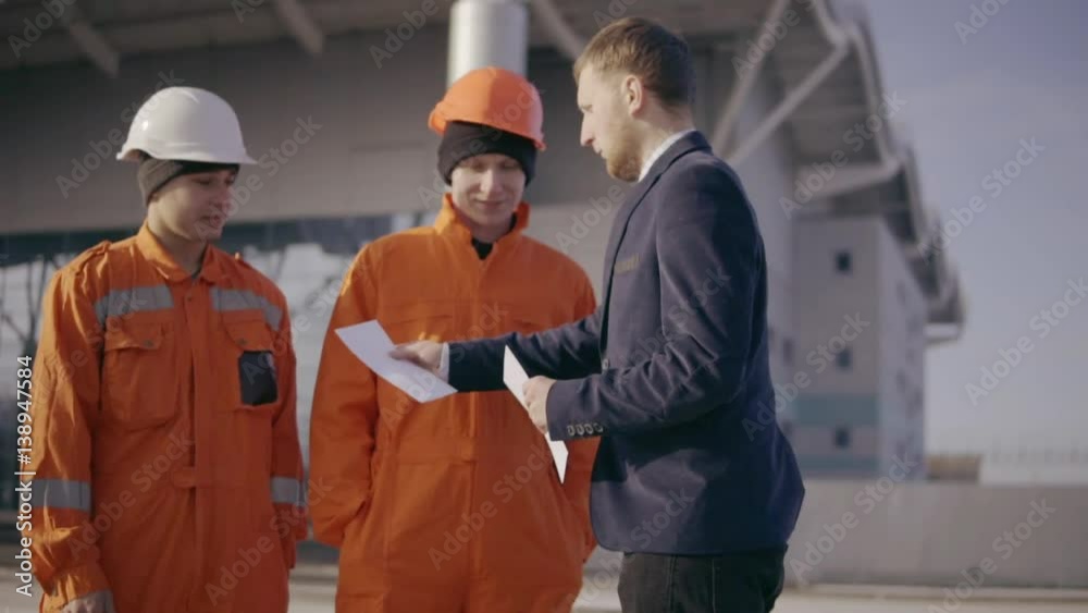 Manager in a suit giving envelopes with money to workers in orange uniform and helmets. Successful finish of the project. Slowmotion Manager in a suit giving envelopes with money to workers in orange uniform and helmets. Successful finish of the project. Slowmotion