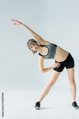 Athletic young woman in sportswear exercising and looking away on grey