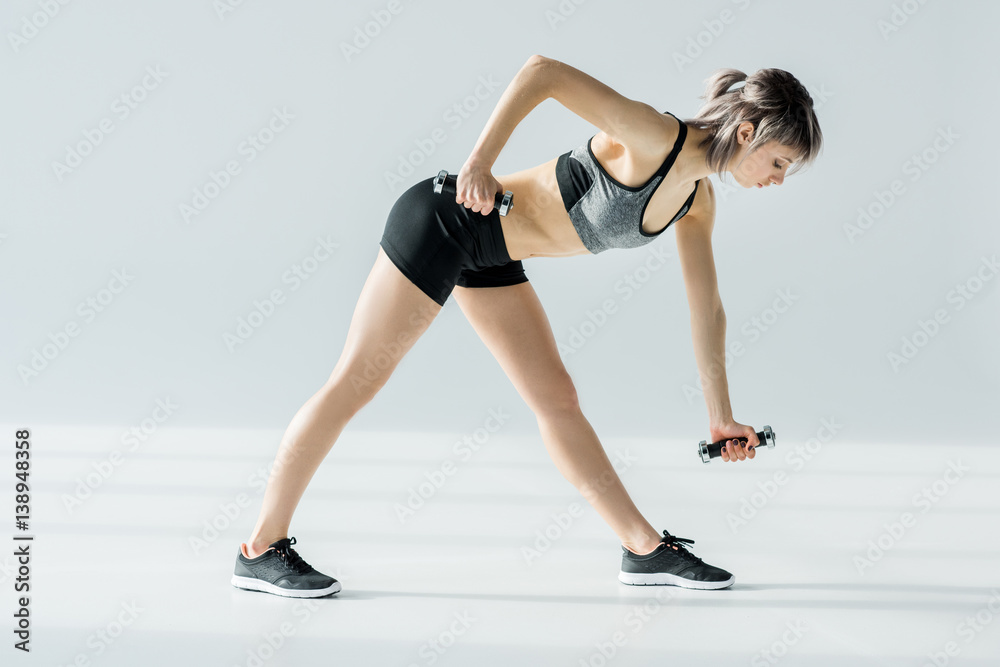 Side view of concentrated young sportswoman training with dumbbells Side view of concentrated young sportswoman training with dumbbells