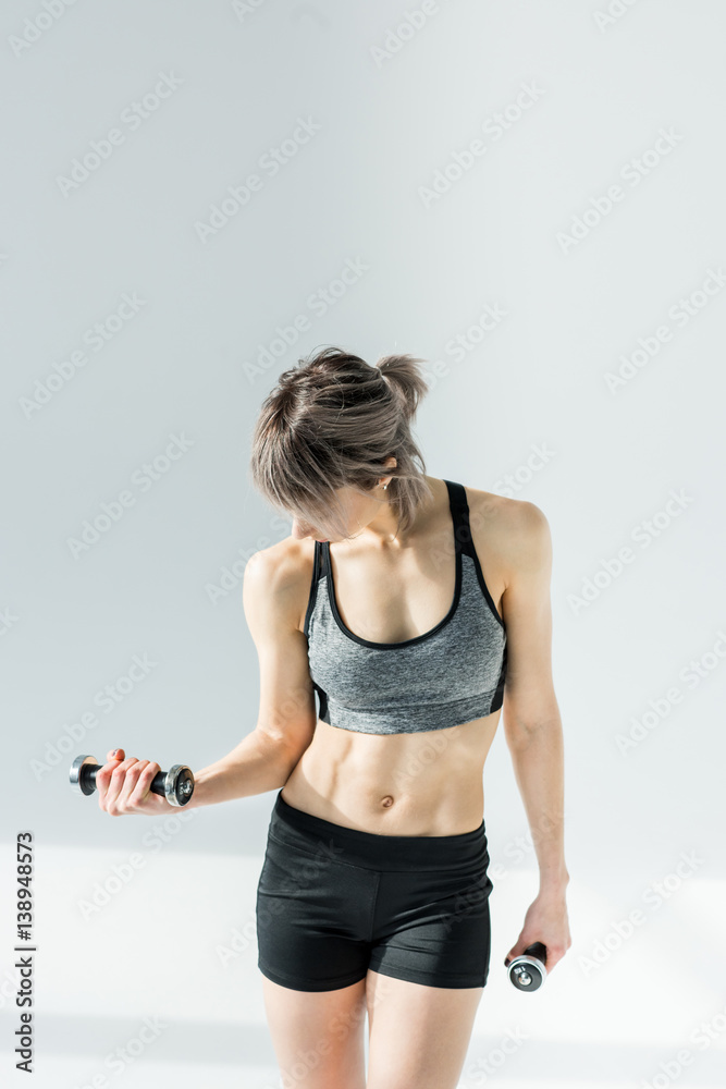 Young sporty woman exercising with dumbbells on grey Young sporty woman exercising with dumbbells on grey