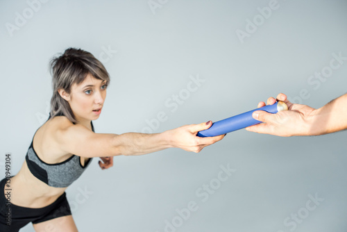 partial view of sportswoman passing relay baton to partner on grey