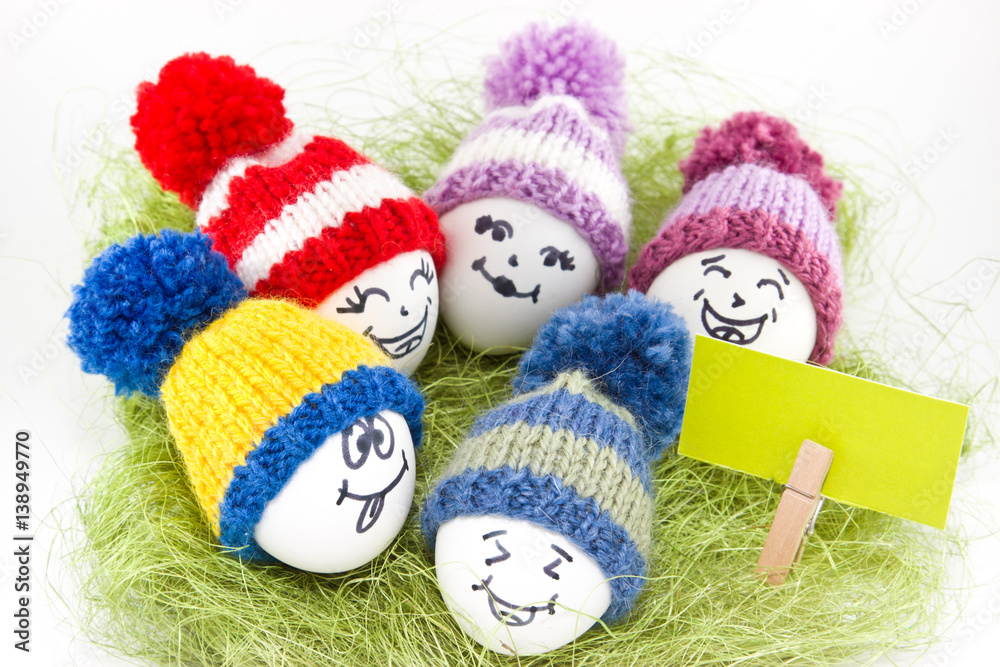 Easter eggs on green sisal. Emoticons in knitted hat with pom-poms. Handmade.