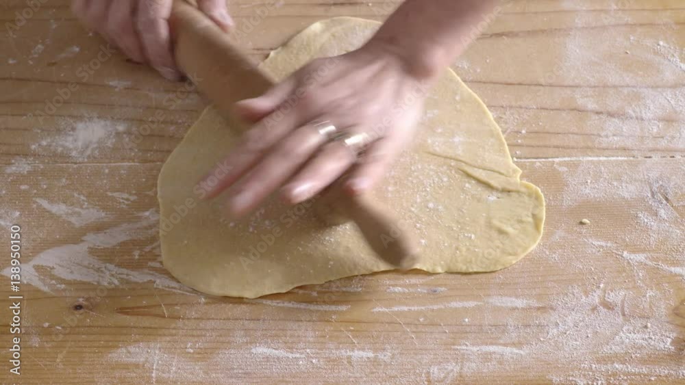 Woman hands with rolling pin that rotates on fresh pasta