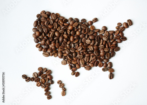 Closeup above view shot: heap of rich brown freshly roasted coffee seeds scattered on white table in shape of world map with continents