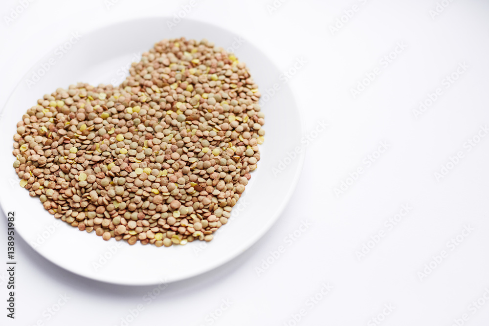 Closeup shot of ripe lentil seeds laid out in shape of heart on white porcelain plate Closeup shot of ripe lentil seeds laid out in shape of heart on white porcelain plate