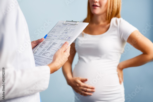 Mid-section image of young pregnant woman talking to doctor in office, focus on folder with patients details in gynecologists hands