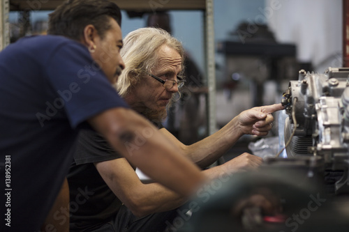 Two mechanics working on motorcycle engine in workshop