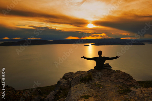 Man sitting on edge of cliff at sunset on Isla Amantani on Lake Titicaca - arms wide open