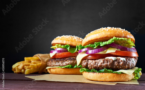 Two craft beef burgers and french fries on wooden table isolated on black background.