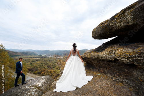 beautiful and young bride in white dress standing near big stone