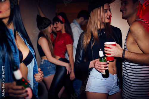 Canvas Print Sneak shot of crowded dark club, young people partying and drinking beer with tw