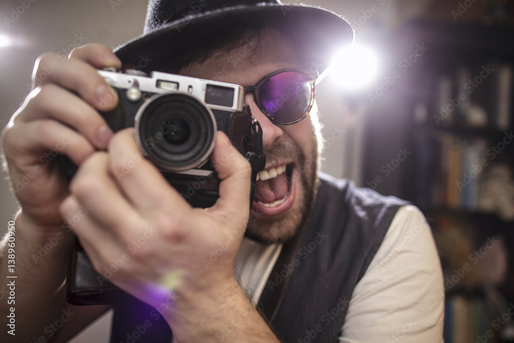 happy smiling photographer hipster wearing sunglasses and hat taking pictures using old style retro camera