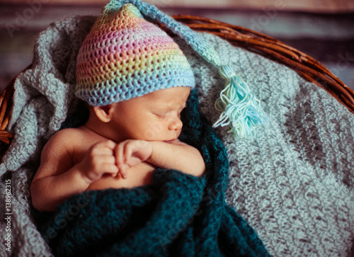 Little child in colorful hat sleeps under green scarf in the basket photo