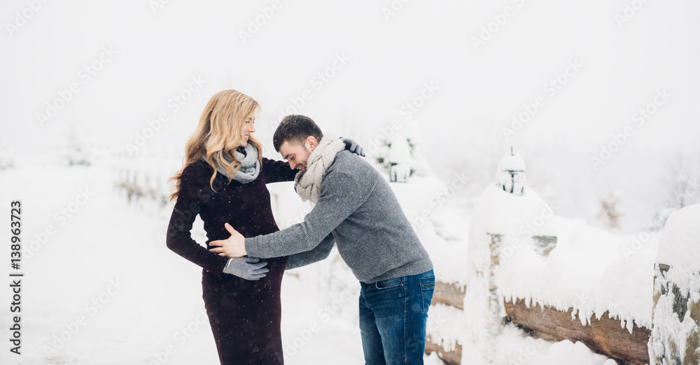 Man touches woman's pregnant belly standing with her on snowy road