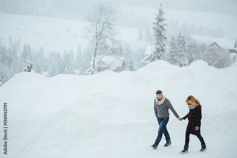 Man and woman hold each other hands walking around snowy road