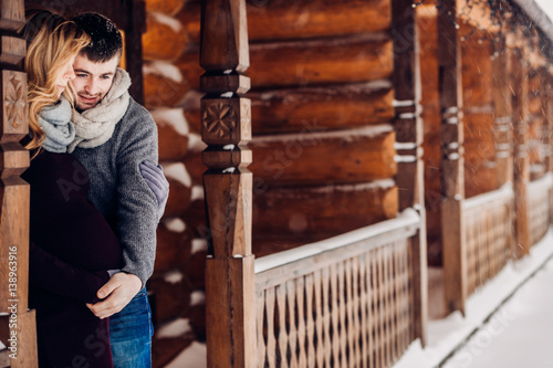 Man lies his hand on woman's expacting belly while they stand on snowy wooden porch photo