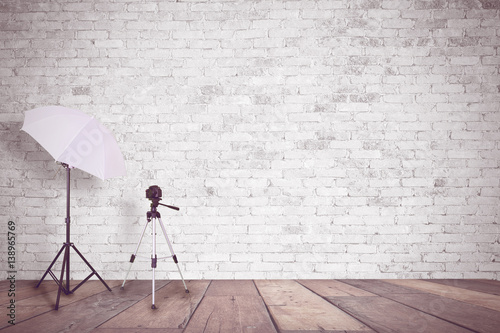 White brick wall in a photo studio. An umbrella for illumination and a tripod for a camera. Empty copy space for Editor's content.