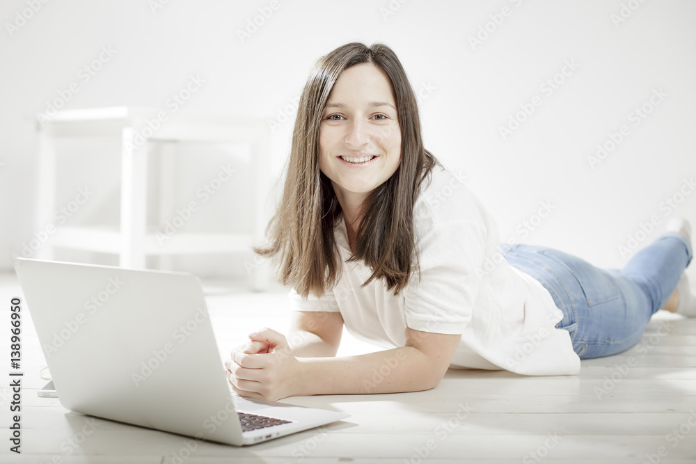 beautiful young girl lying on the floor with a laptop and smiling, dressed in a white shirt with short sleeves and jeans beautiful young girl lying on the floor with a laptop and smiling, dressed in a white shirt with short sleeves and jeans