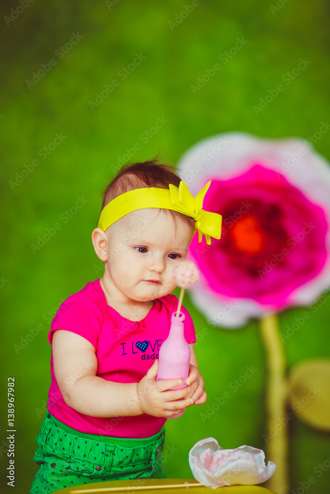 Curious child with yellow bow on her head looks at ball in pink bottle