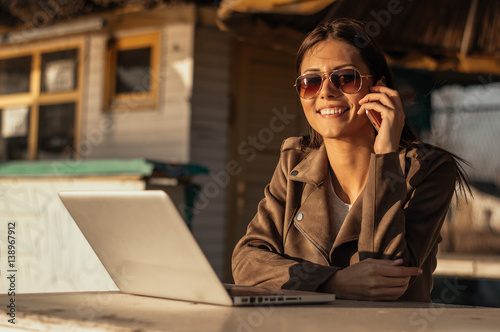 Girl talking on the phone while working on computer outdoor