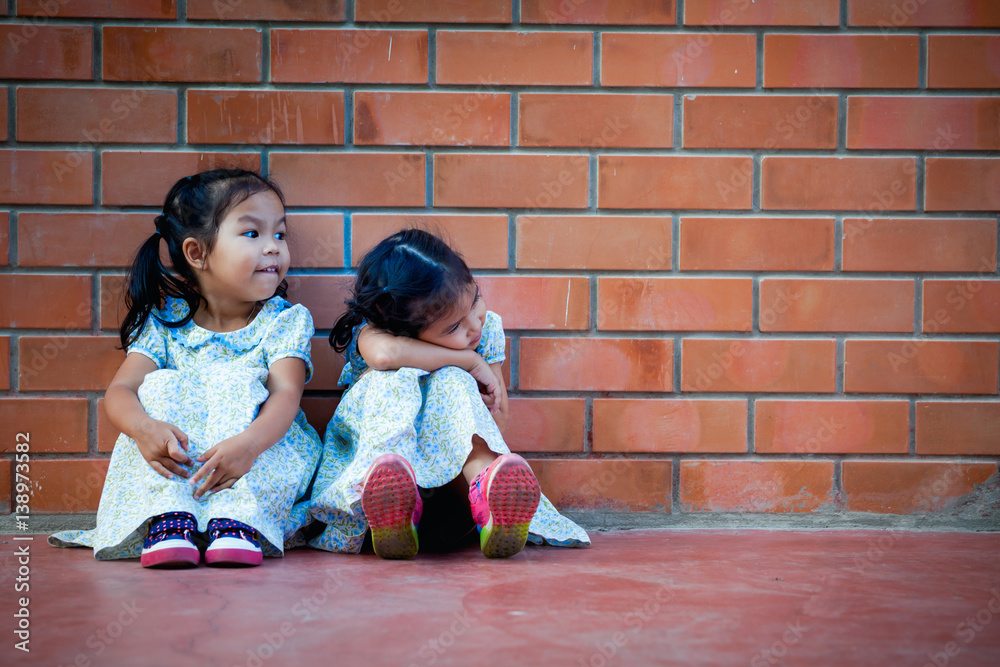 Asia little girl sitting with friend on brick wall background Asia little girl sitting with friend on brick wall background