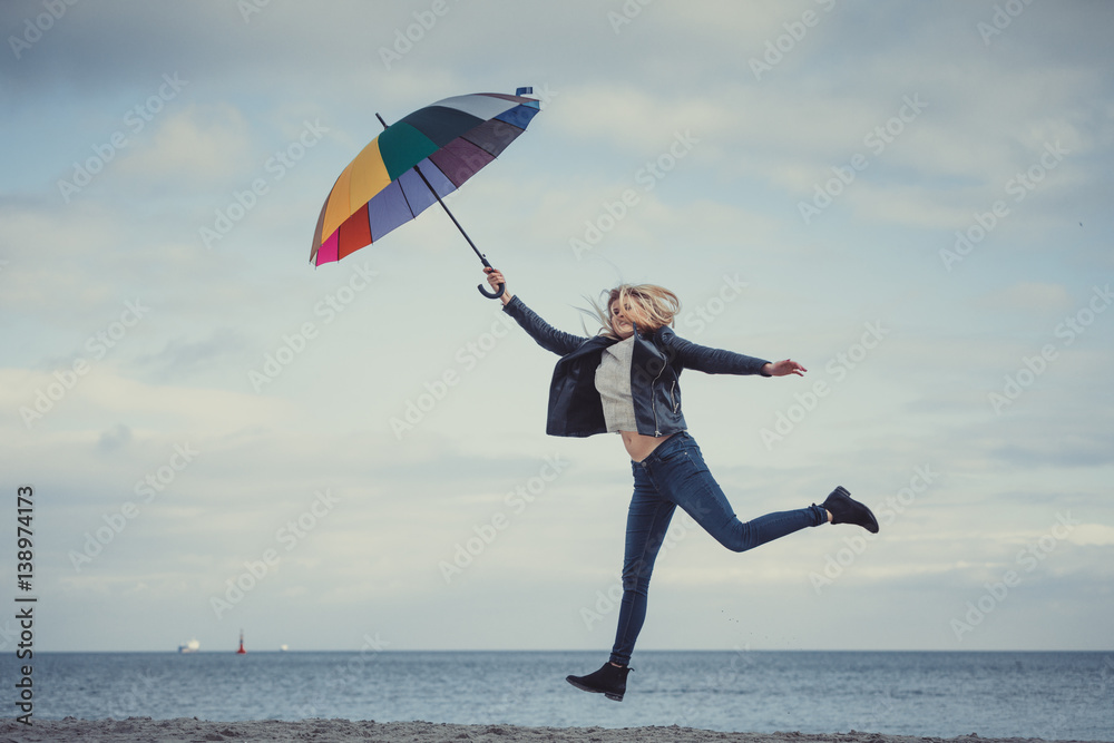Woman jumping with colorful umbrella on beach Woman jumping with colorful umbrella on beach