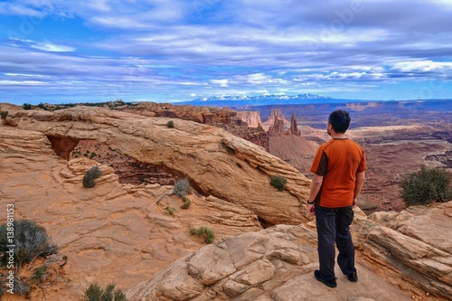 Man hiker on cliff in rock desert. Mesa Arch in Canyonlands National Park. La Sal Mountains. Moab. Cedar City. Utah. United States.