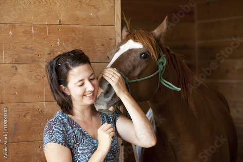 Smiling woman with horse in barn, closeup
