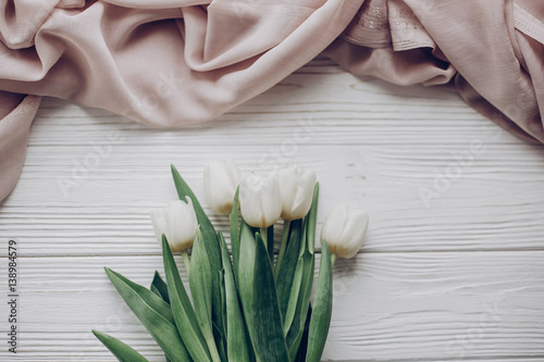 hello spring flat lay. stylish white tulips and beige soft fabric on rustic wooden table background top view. soft light  tenderness atmospheric moment. space for text. rustic wedding