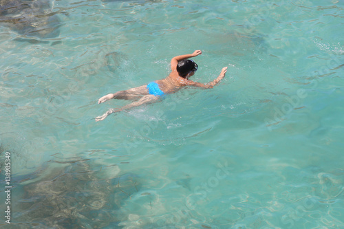 Boy in a mask floats in a transparent greenish water sea lagoon.