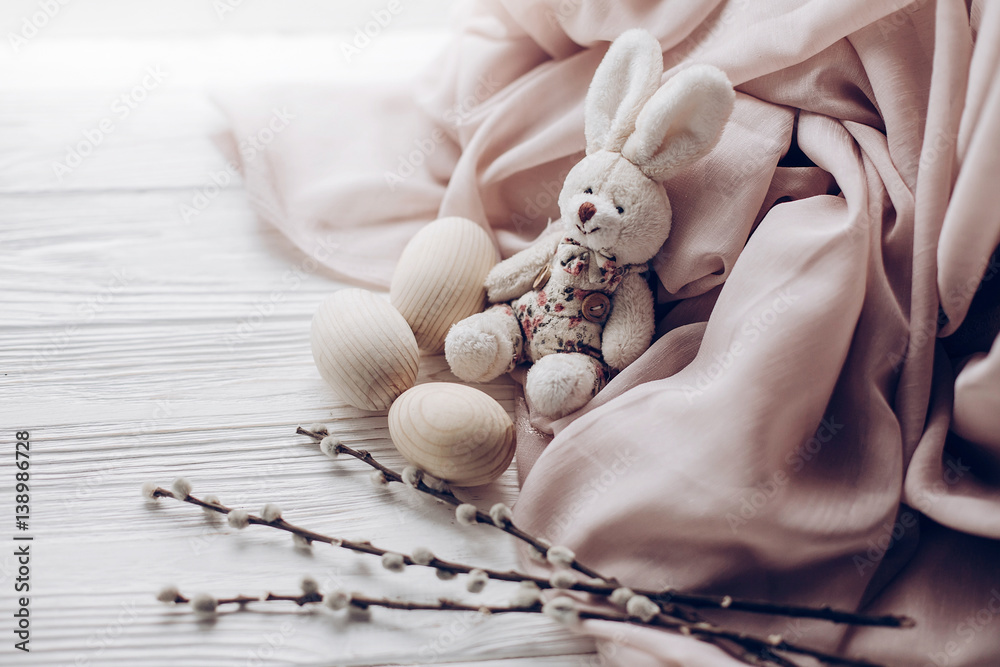 stylish easter bunny rabit and eggs and willow buds on rustic wooden background and fabric . greeting card concept with space for text, top view. soft light